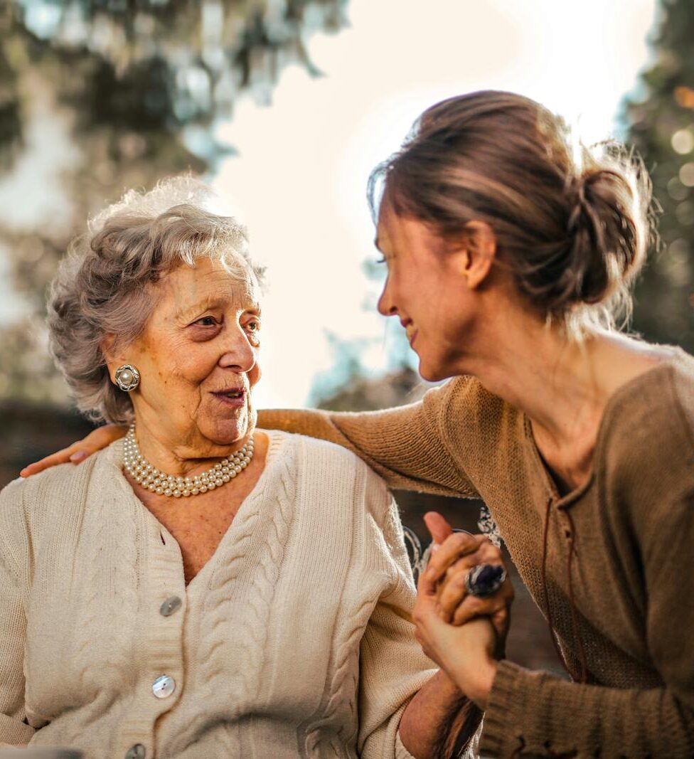 Elderly woman and adult daughter share a joyful, affectionate moment in a sunny garden.